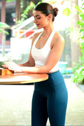 Woman in blue leggings sitting outdoors with greenery in background