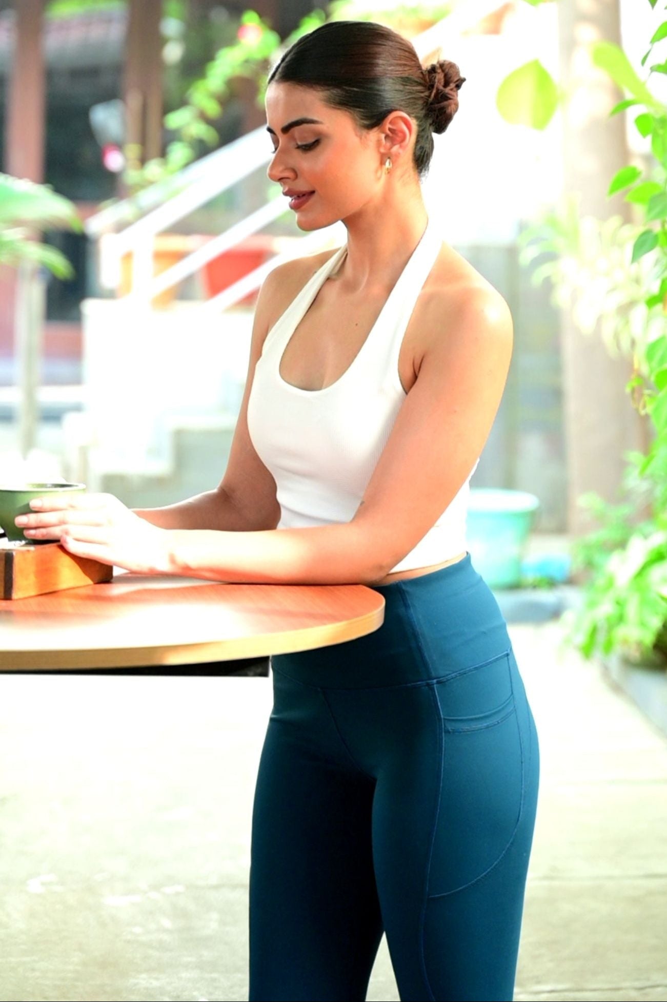 Woman in blue leggings sitting outdoors with greenery in background